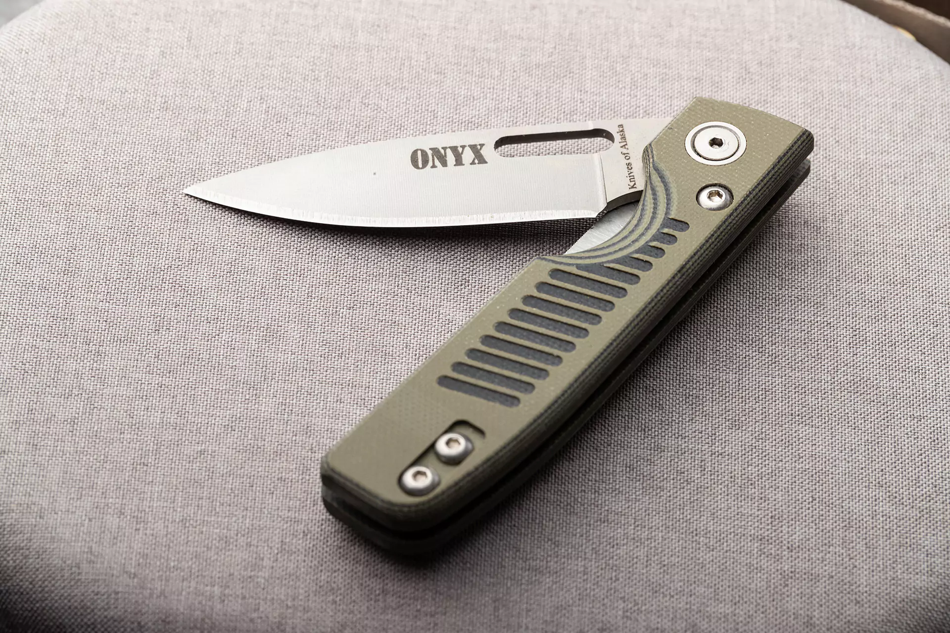 Onyx folding knife with OD green G10 handle and MagnaCut blade resting on light fabric