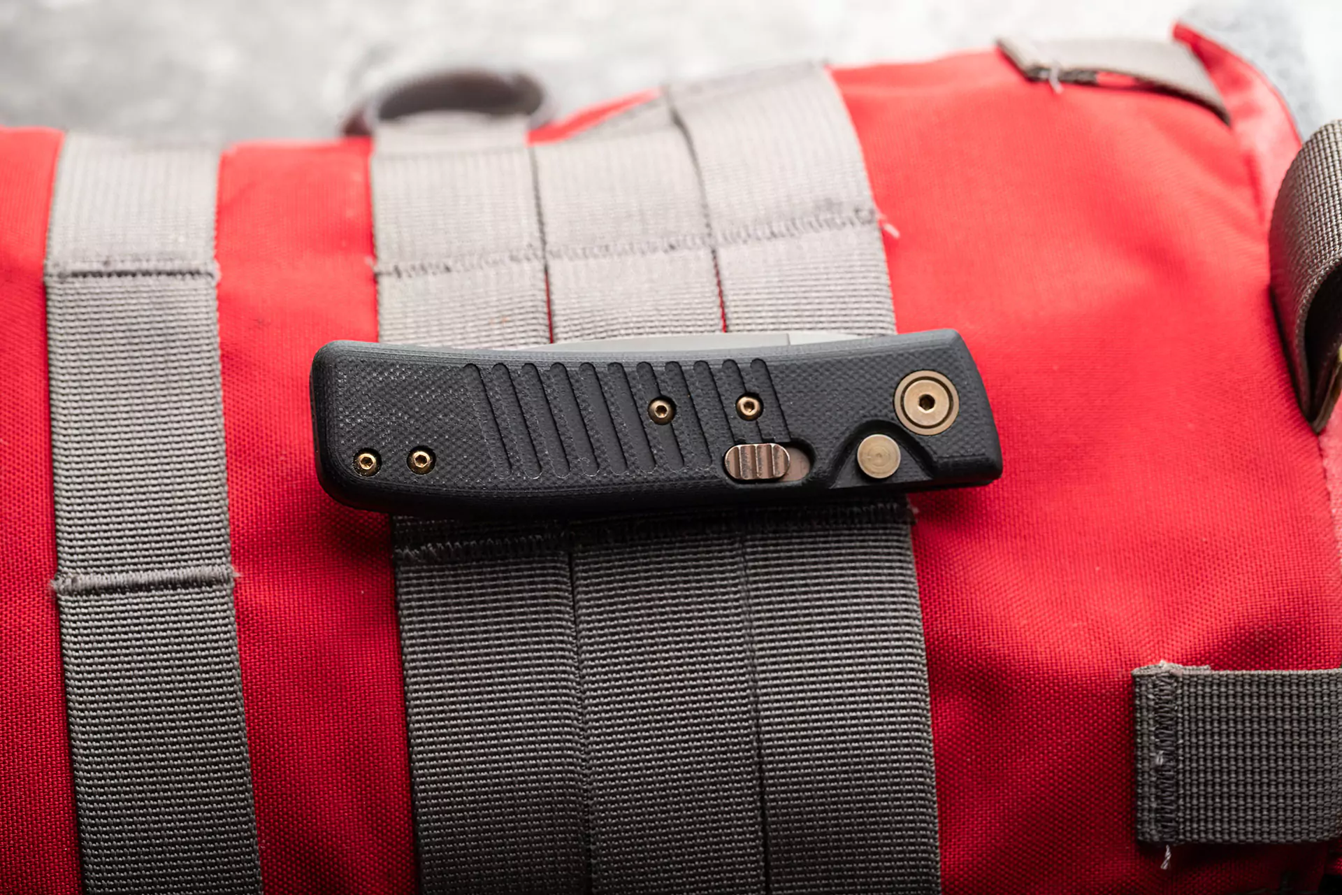 Onyx Auto knife with MagnaCut blade and black G10 handle clipped to a red tactical backpack