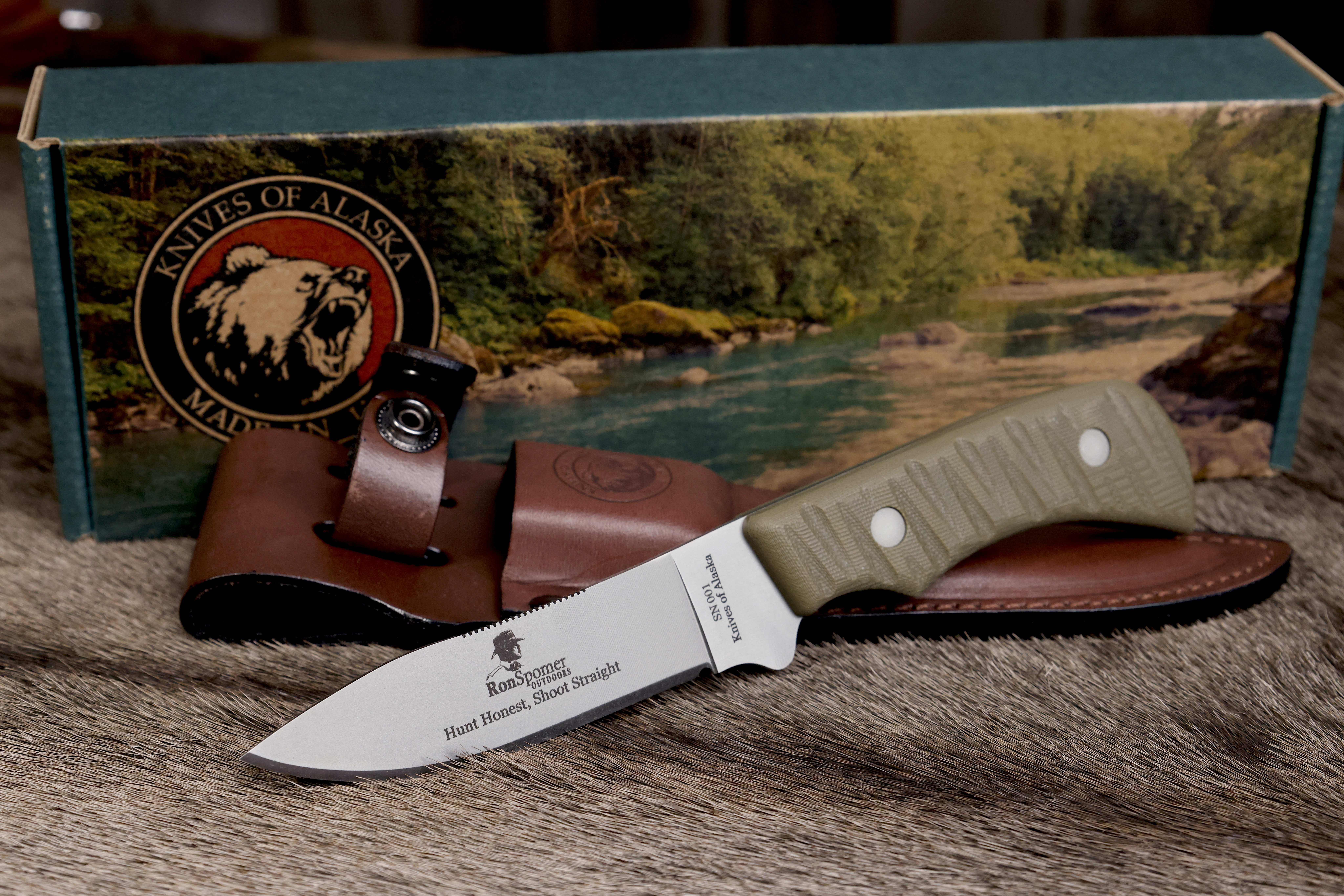 Ron Spomer edition Classic Hunter drop point hunting knife with green textured handle, engraved blade, leather sheath, and Knives of Alaska branded box on a natural fur surface.