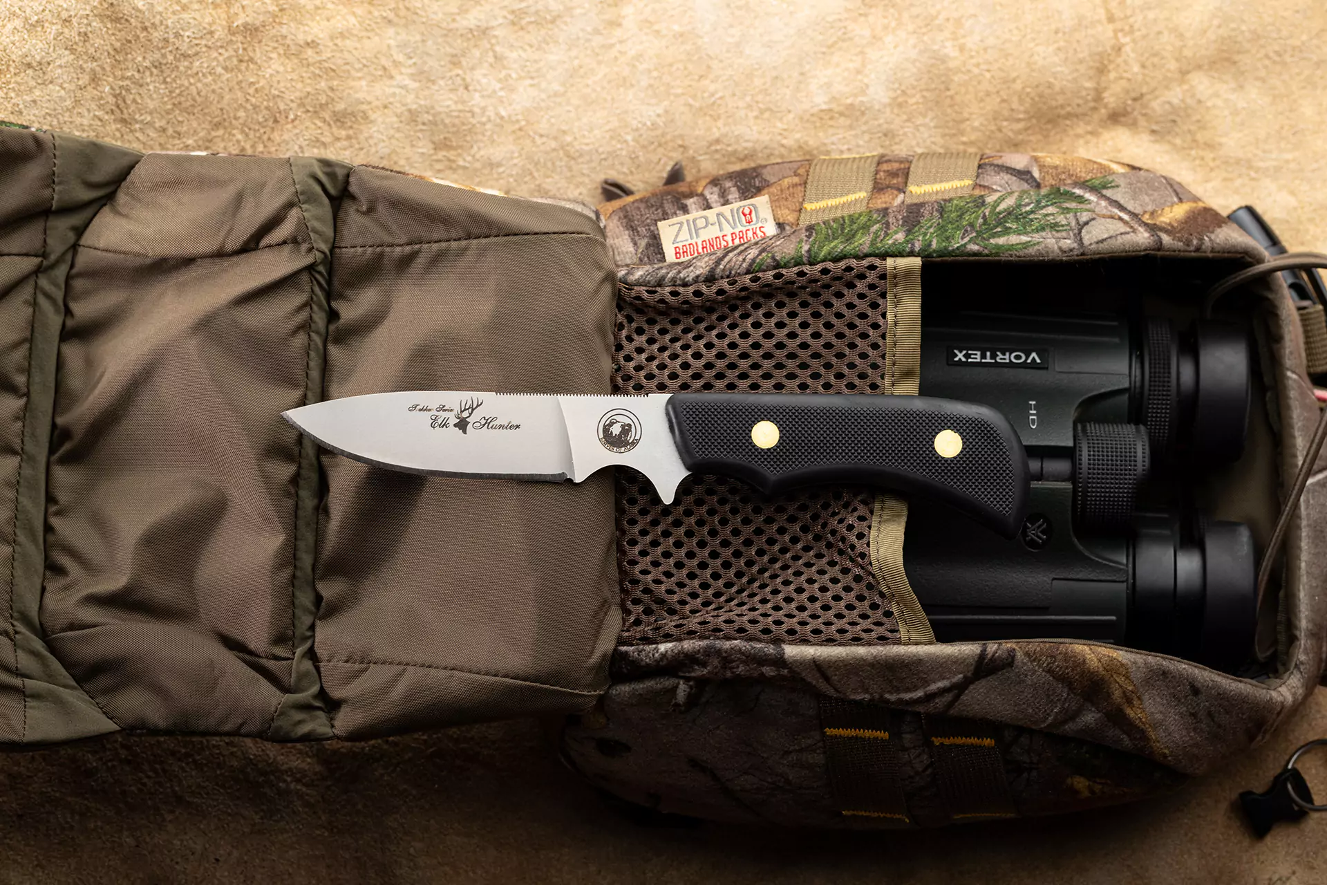 Trekker Elk Hunter knife with Suregrip handle displayed on a camouflage hunting pack with Vortex binoculars