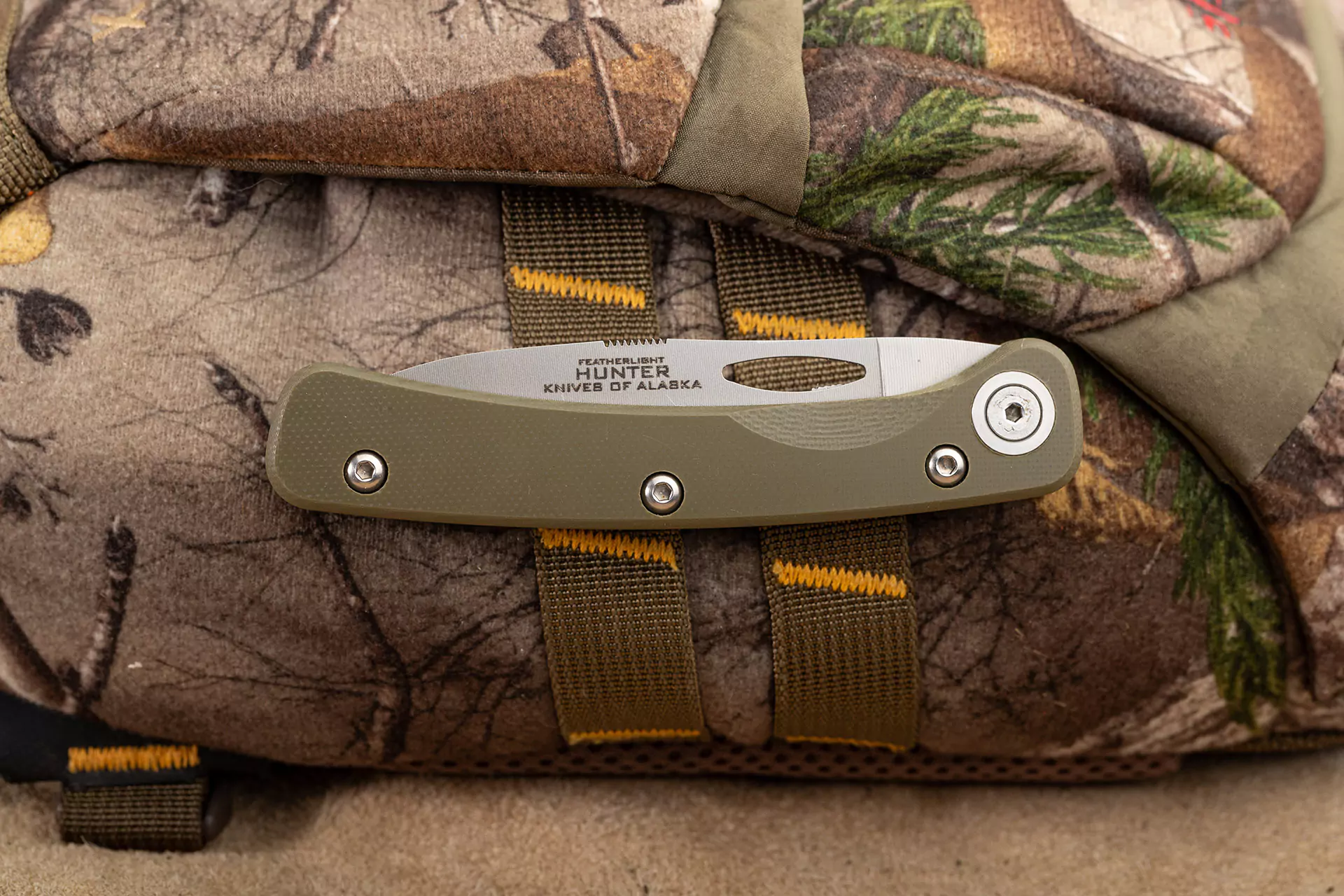 Featherlight drop-point folding knife with OD green G10 handle on camouflage backpack