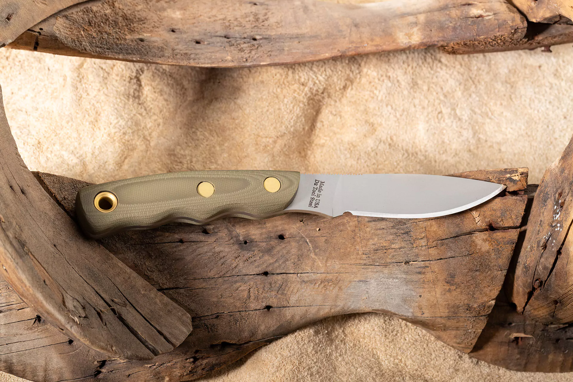 Alpha Wolf knife with OD green G10 handle resting on driftwood