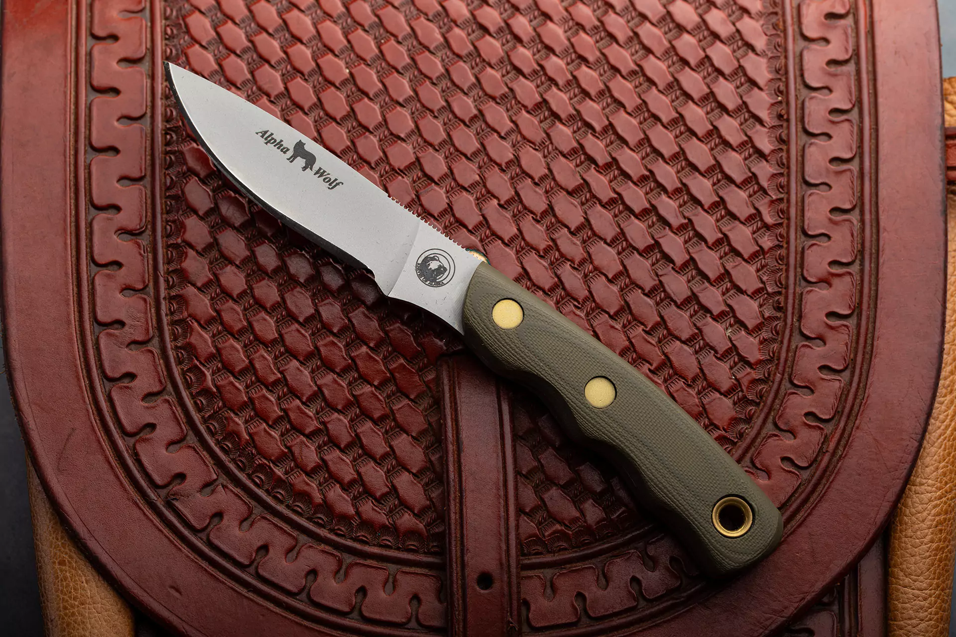 Alpha Wolf knife with OD green G10 handle displayed on tooled leather