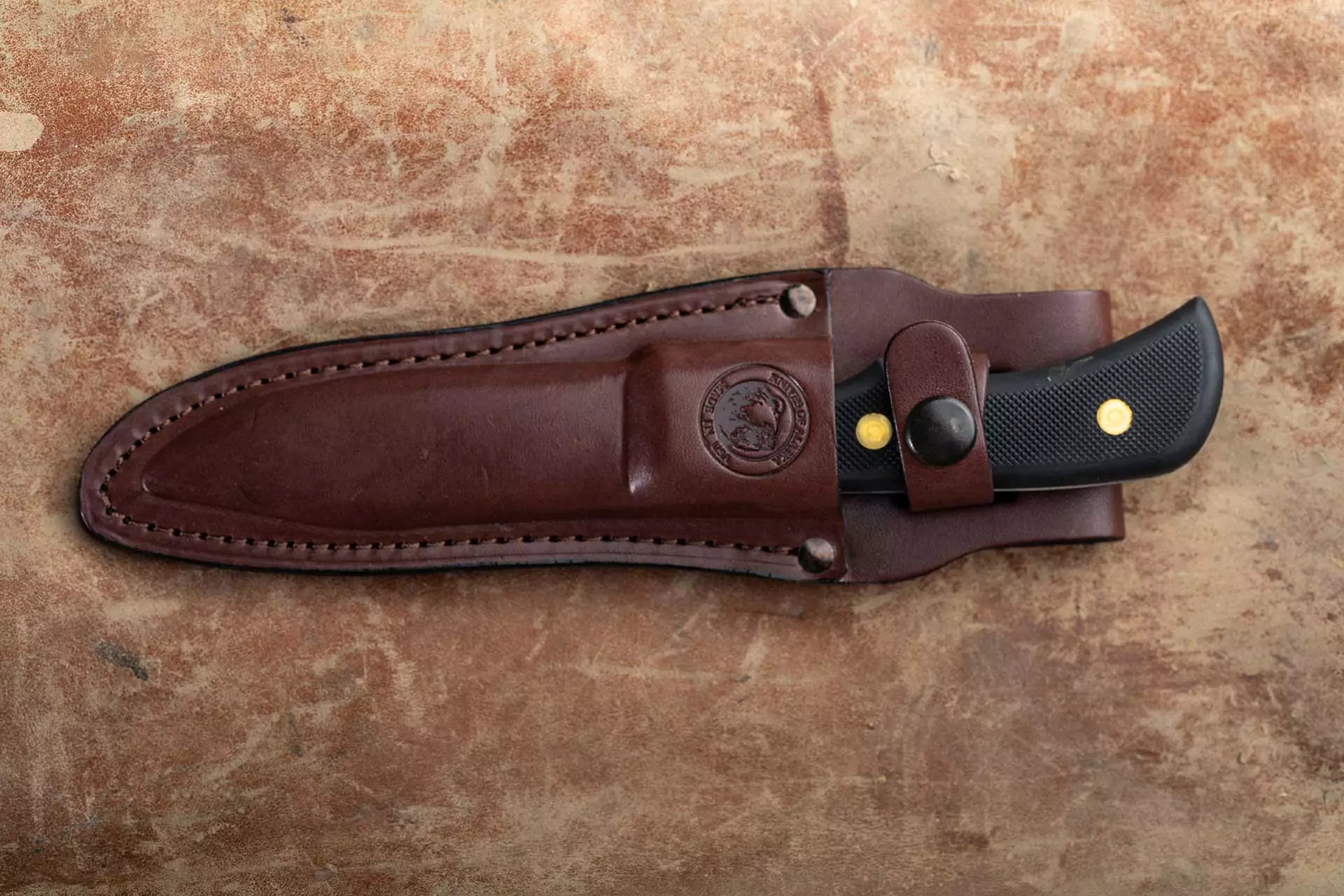 Trekker Whitetail knife in brown leather sheath with black Suregrip handle visible