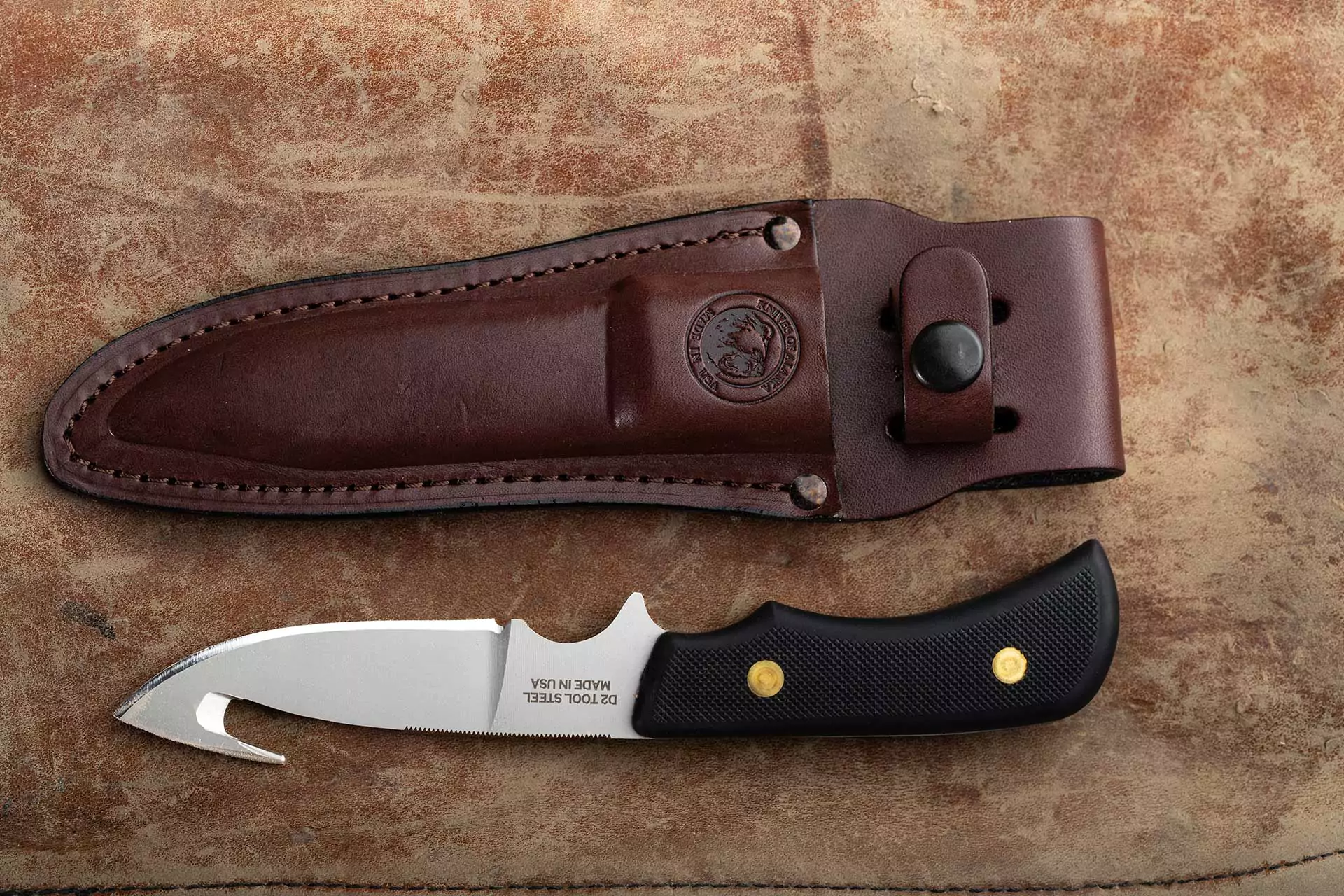 Trekker Whitetail knife with gut hook and Suregrip handle beside a brown leather sheath