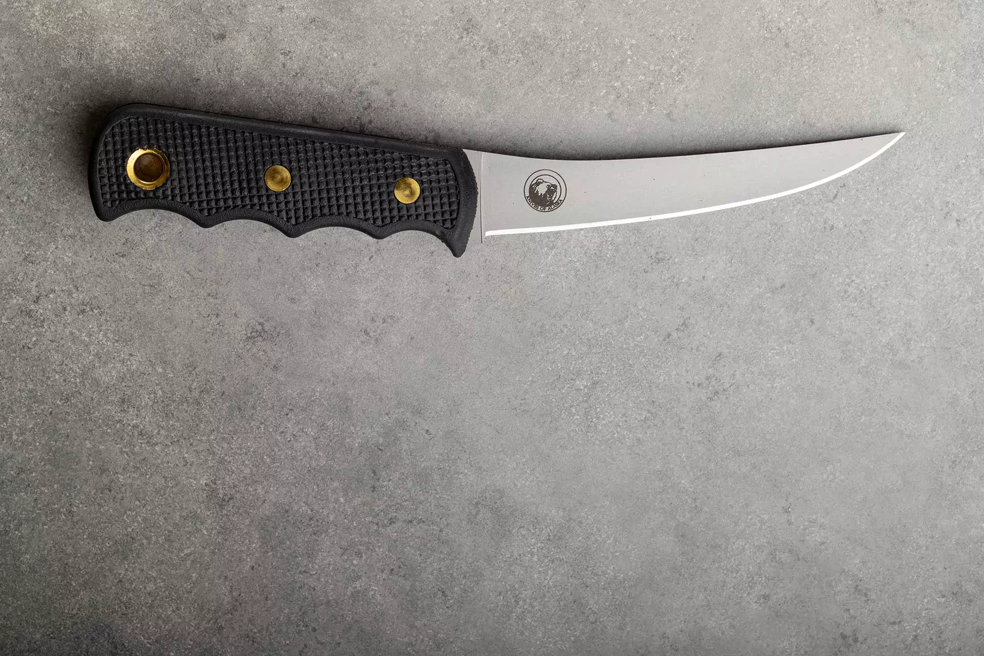 Knives of Alaska professional boning knife with black Suregrip handle and semi-flexible D2 steel blade on stone background