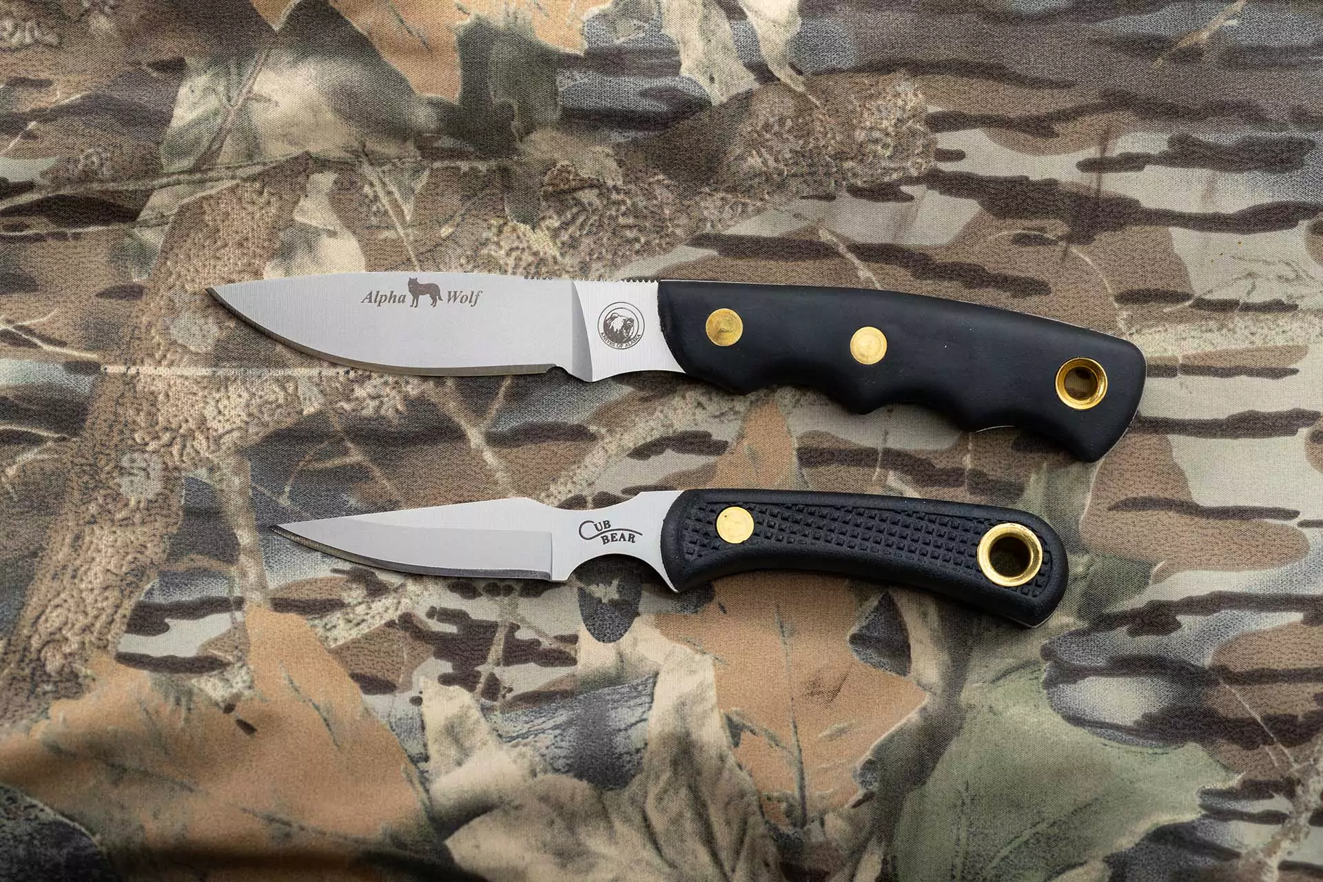 Alpha Wolf and Cub Bear knives with Suregrip handles on camouflage background