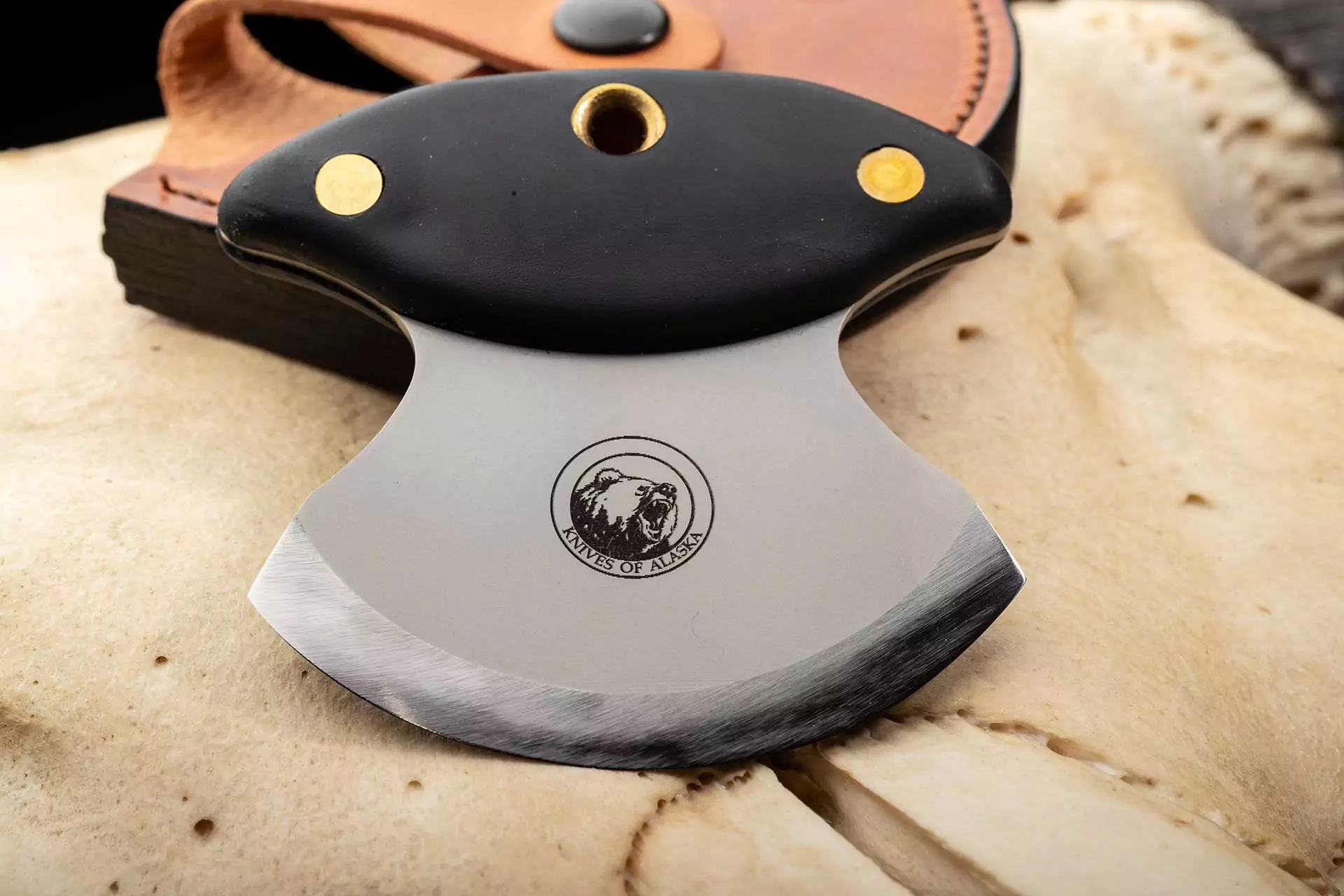 Magnum Ulu knife with Suregrip handle and leather sheath on dark fur