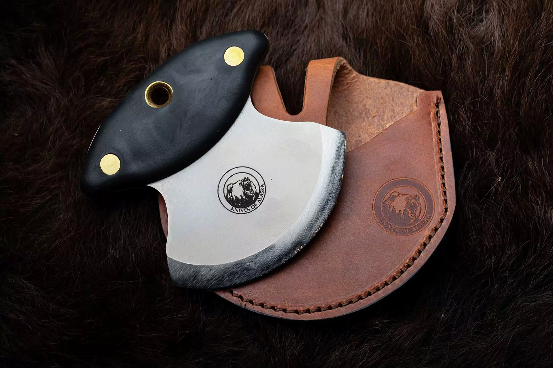 Magnum Ulu knife with Suregrip handle and leather sheath on dark fur