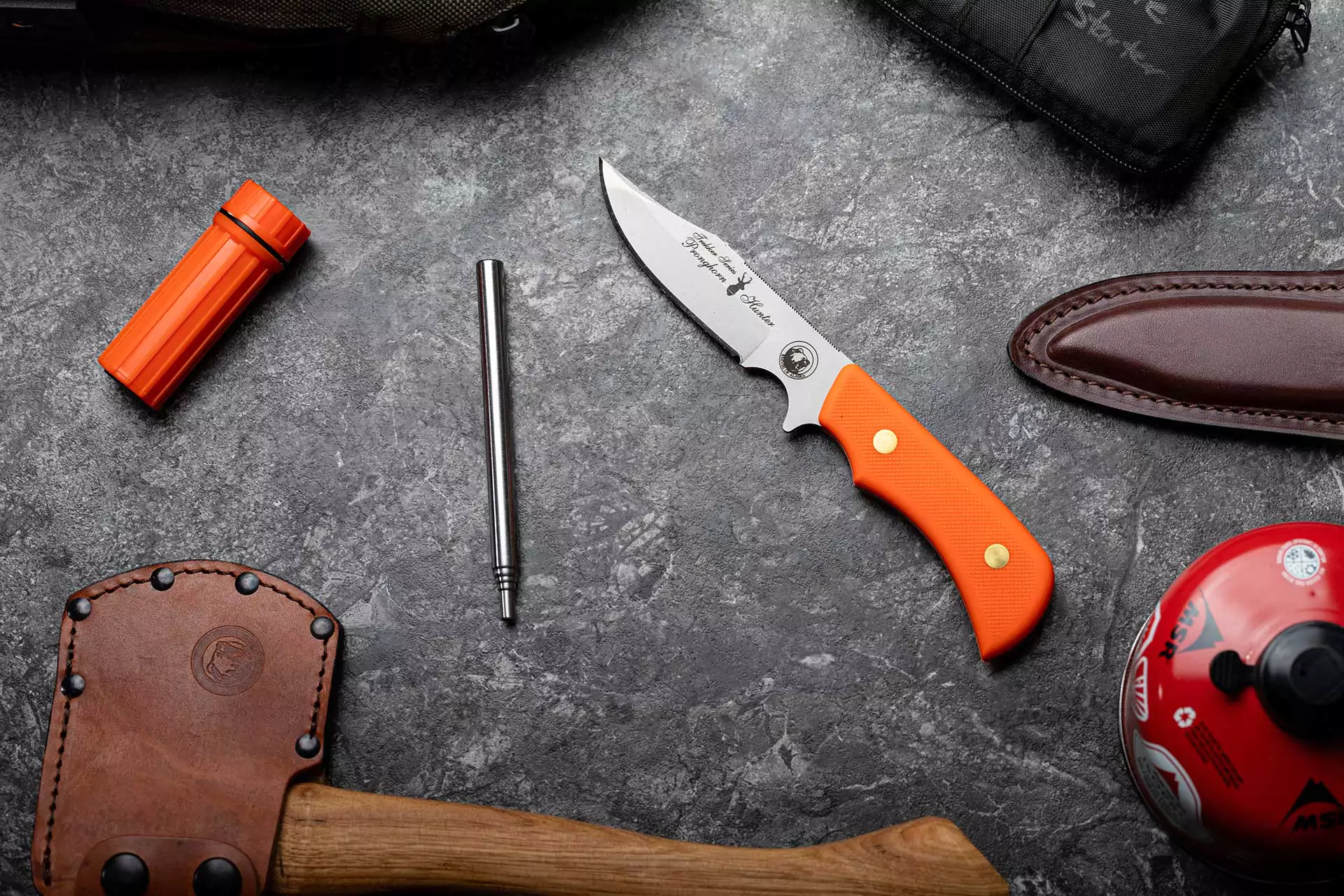 Trekker Pronghorn hunting knife with orange handle displayed among survival gear