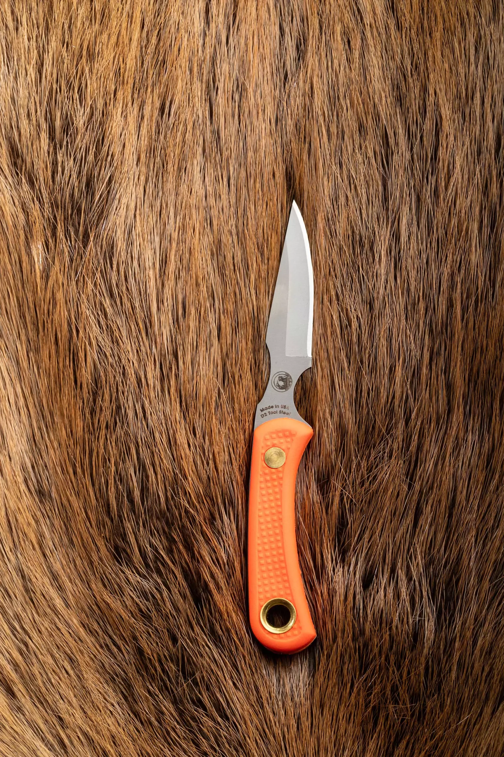 Cub Bear knife with orange Suregrip handle resting on brown animal hide