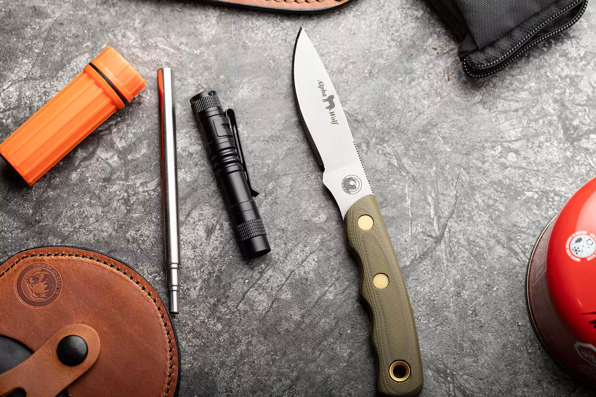 Alpha Wolf knife with OD green G10 handle beside firestarter and flashlight