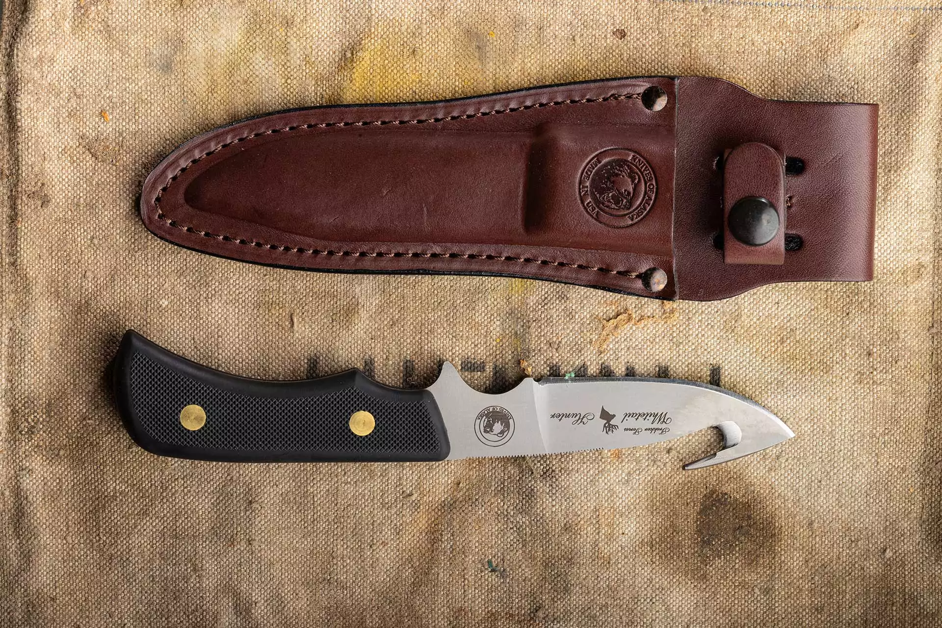 Trekker Whitetail knife with gut hook and Suregrip handle beside leather sheath