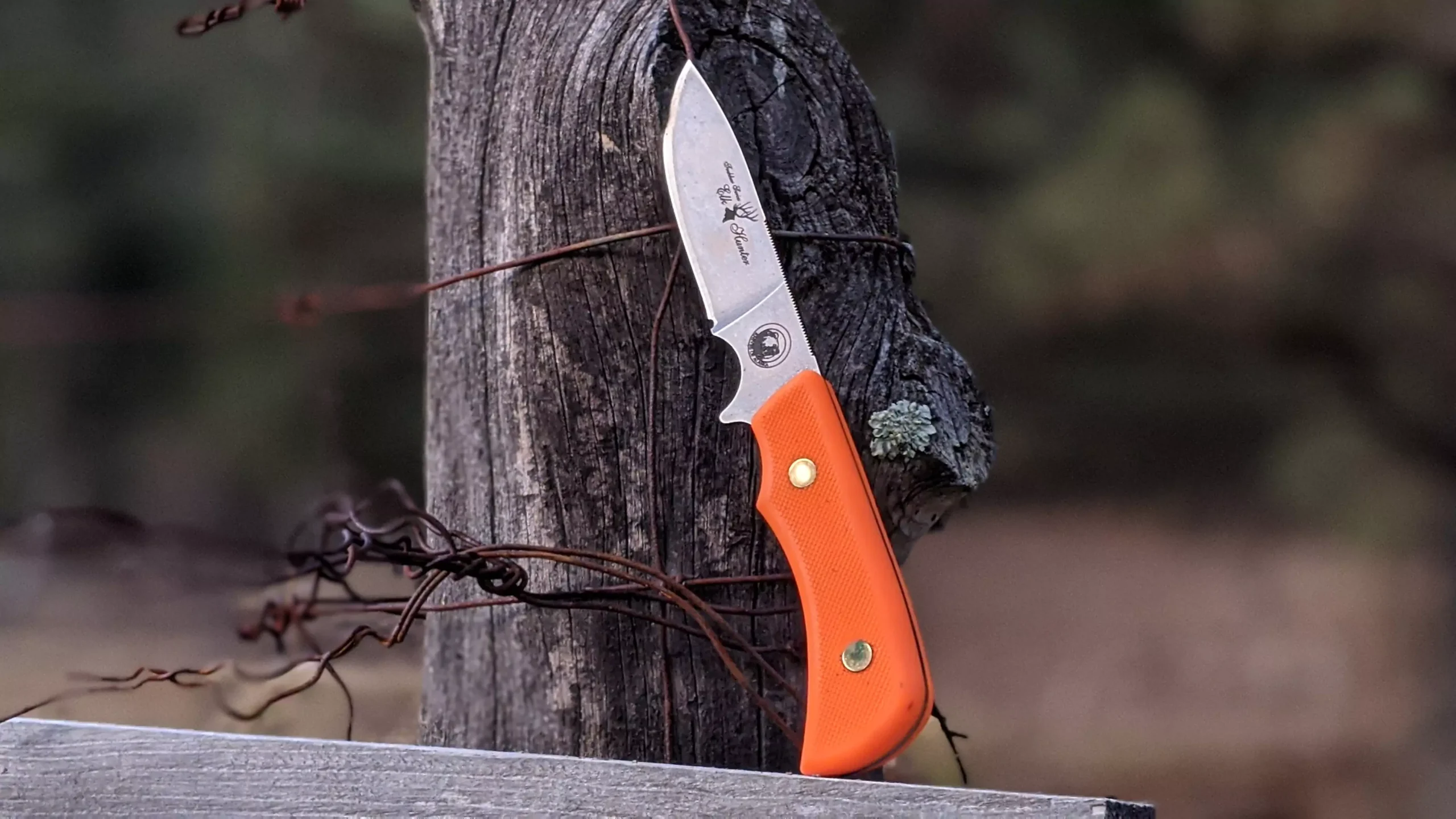 Trekker Elk Hunter knife with orange SureGrip handle stuck in weathered wood fence
