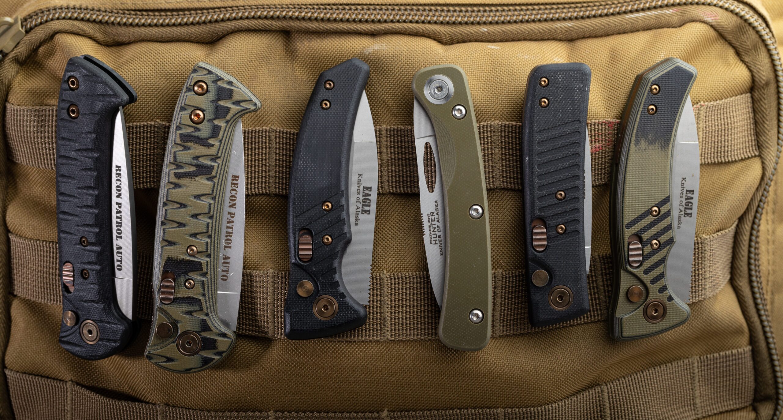 Lineup of Knives of Alaska everyday carry and hunting folding knives secured to a tactical tan backpack, including Recon Patrol Auto, Eagle, and Hunter models.