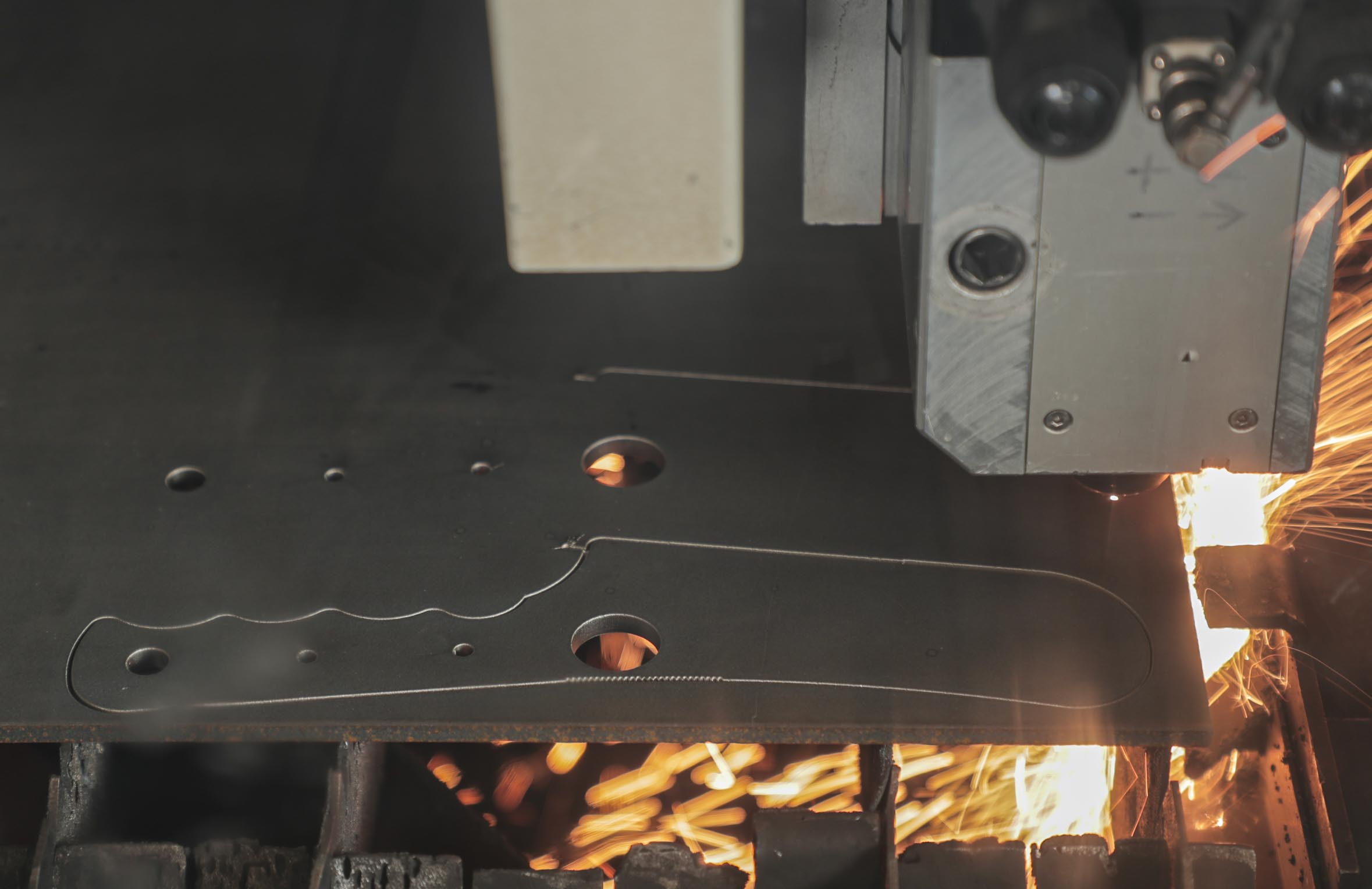 Precision laser cutting high-quality steel during the Knives of Alaska manufacturing process, forming knife blade and handle profiles with sparks flying.
